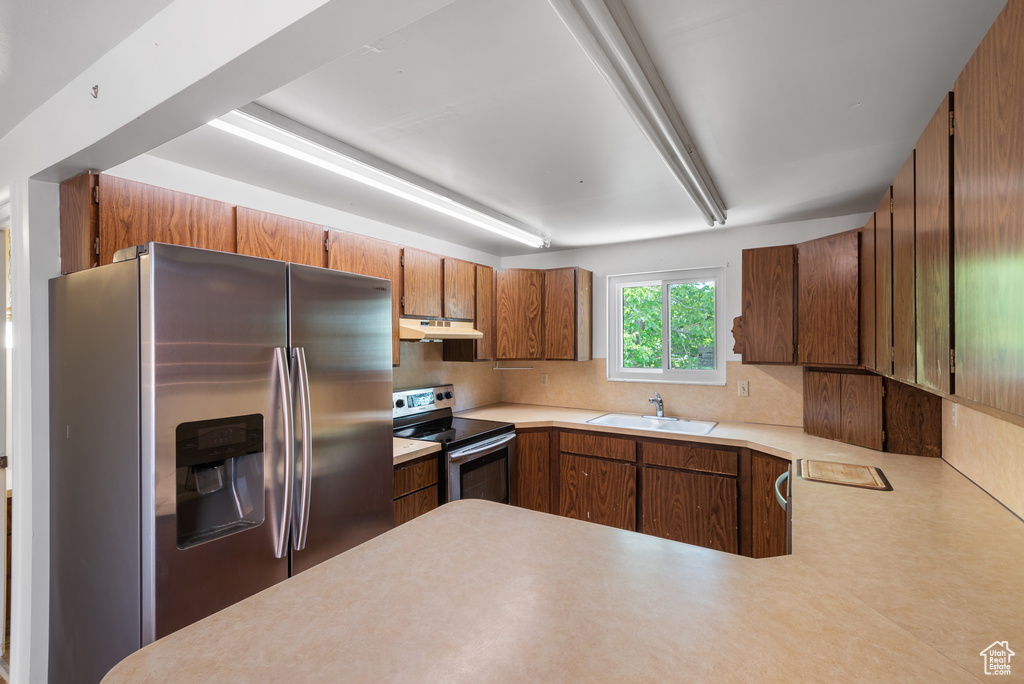 Kitchen featuring stainless steel appliances, under cabinet range hood, a sink, decorative backsplash, and light countertops