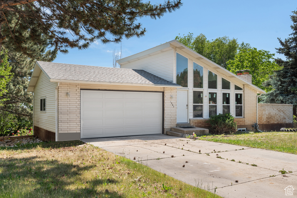 Mid-century home with a garage, concrete driveway, brick siding, and a chimney