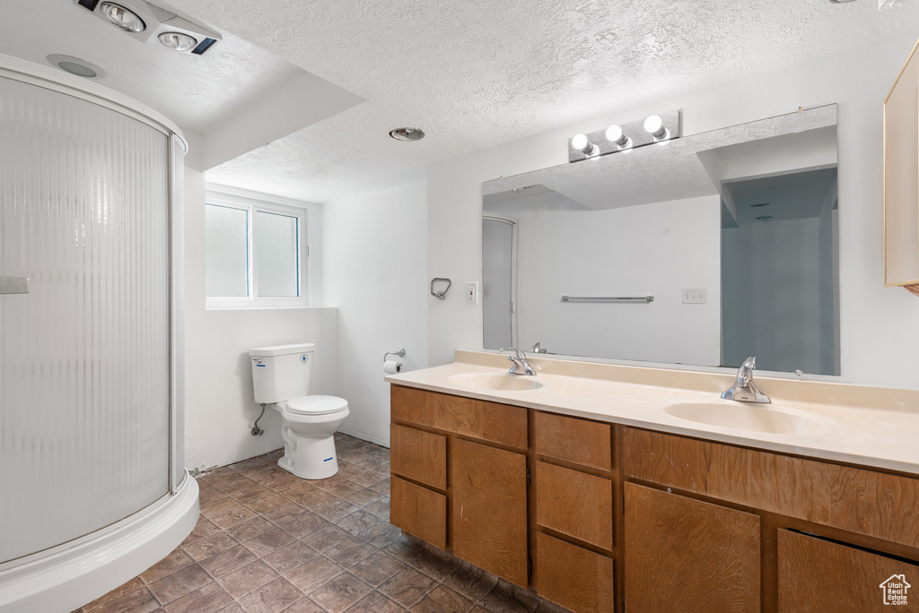 Full bathroom with a stall shower, double vanity, a textured ceiling, and toilet