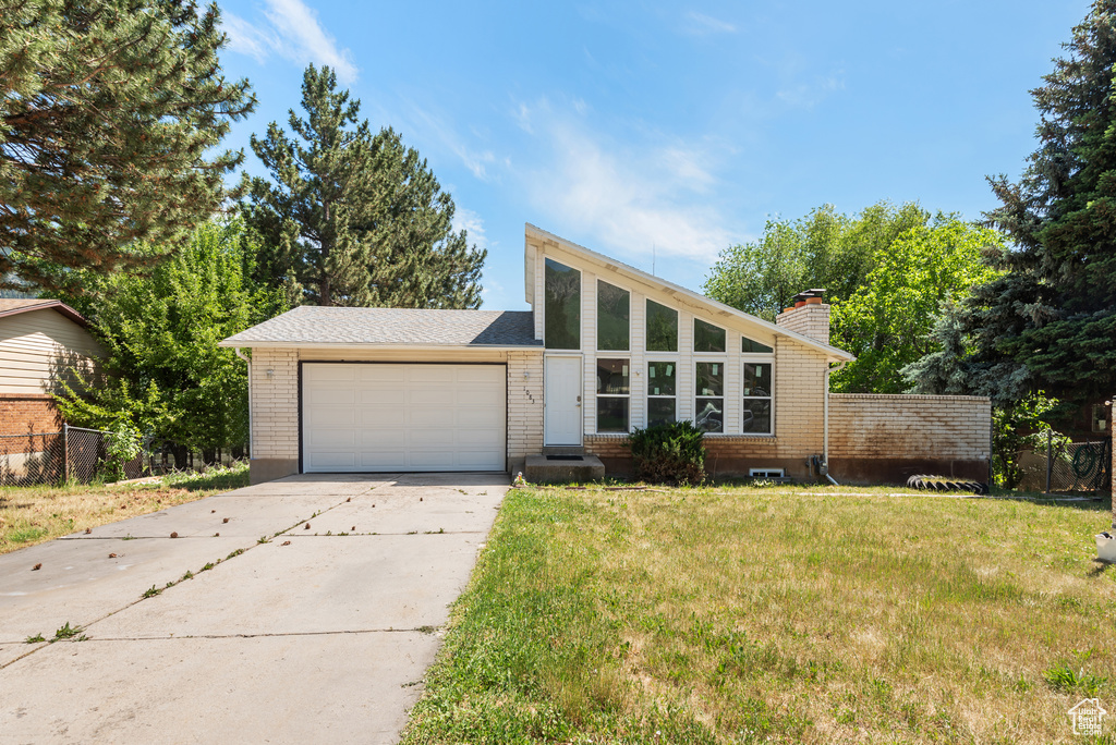 Mid-century home with a garage, concrete driveway, a front lawn, a chimney, and brick siding