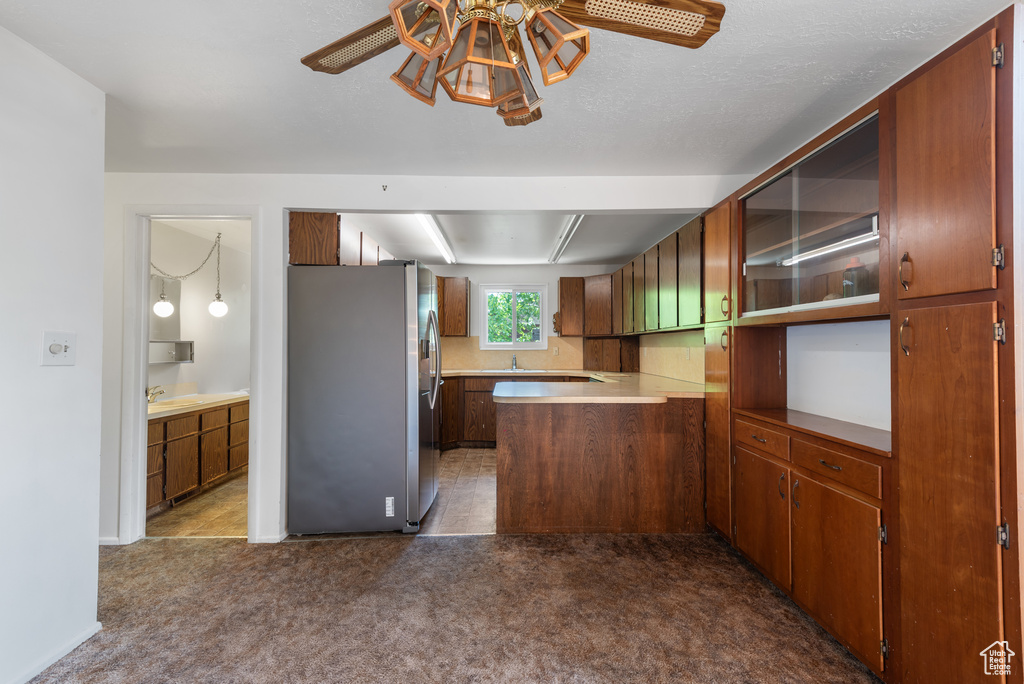 Kitchen featuring freestanding refrigerator, a peninsula, ceiling fan, light countertops, and dark colored carpet