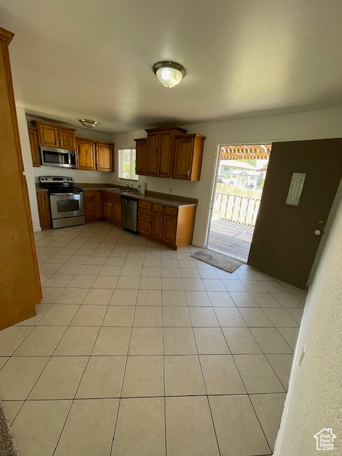 Kitchen featuring stainless steel appliances, a sink, dark countertops, brown cabinets, and light tile patterned floors