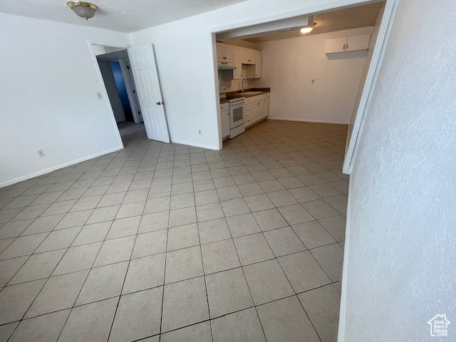 Unfurnished living room featuring a sink, light tile patterned floors, and baseboards