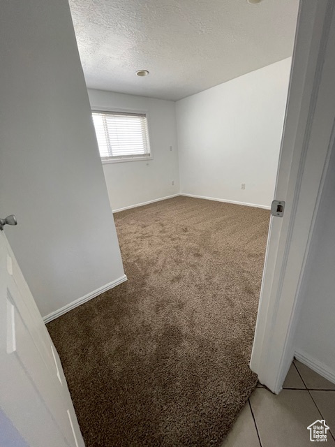 Spare room with a textured ceiling, baseboards, and light colored carpet
