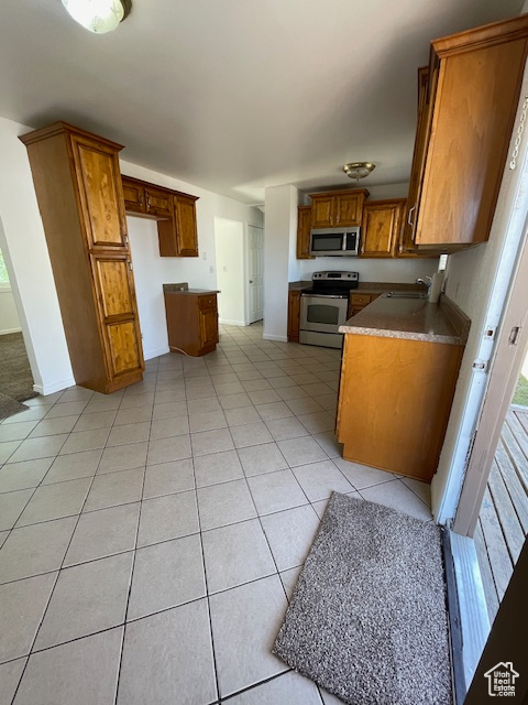 Kitchen with stainless steel appliances, a sink, brown cabinetry, light tile patterned floors, and baseboards
