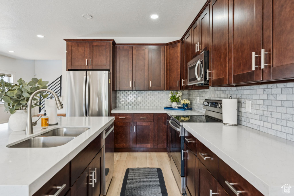 Kitchen with appliances with stainless steel finishes, a sink, light countertops, light wood-style flooring, and recessed lighting