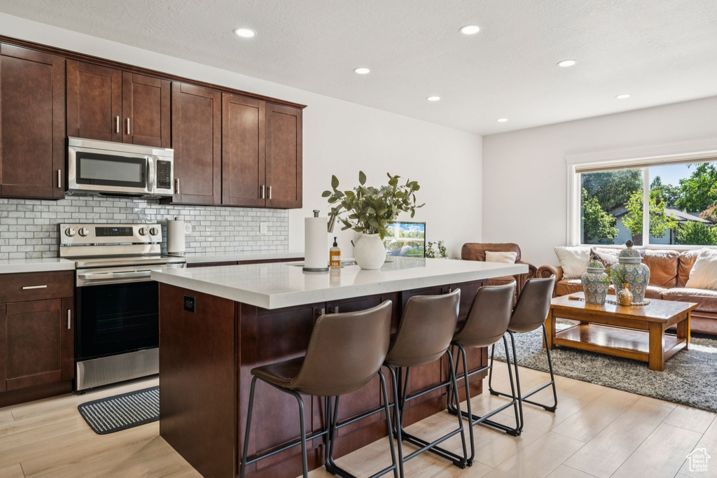 Kitchen featuring appliances with stainless steel finishes, a center island, decorative backsplash, light countertops, and a breakfast bar area