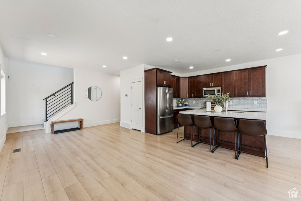 Kitchen with appliances with stainless steel finishes, light countertops, tasteful backsplash, recessed lighting, and light wood-type flooring
