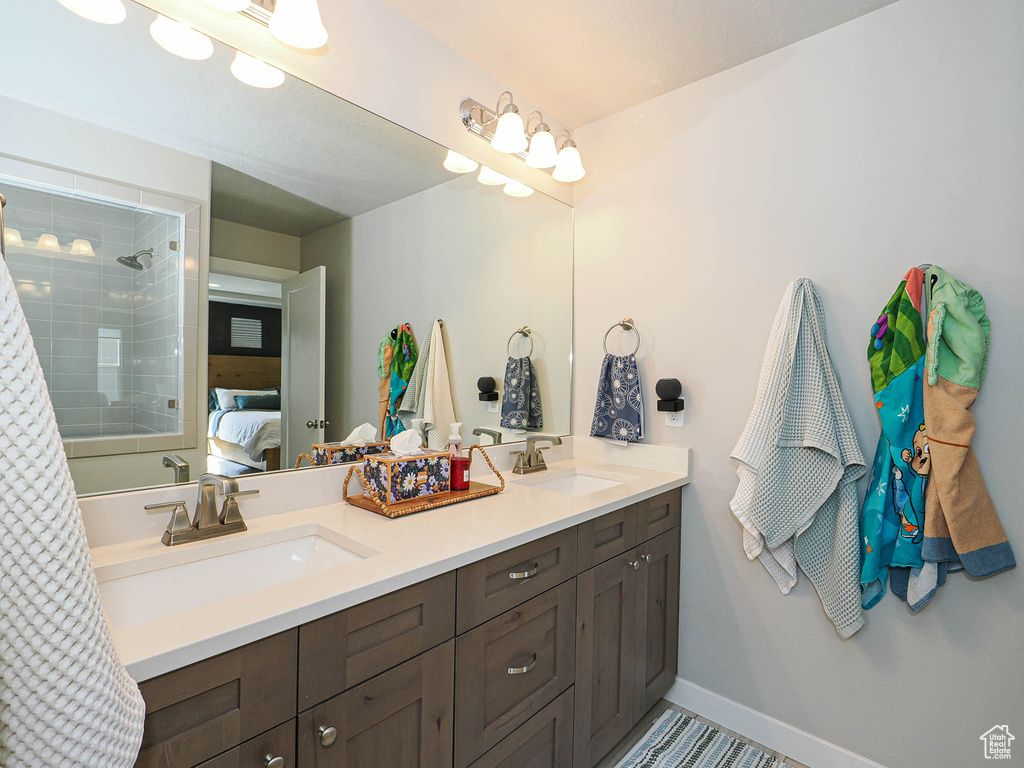 Full bathroom featuring ensuite bath, double vanity, a tile shower, and baseboards