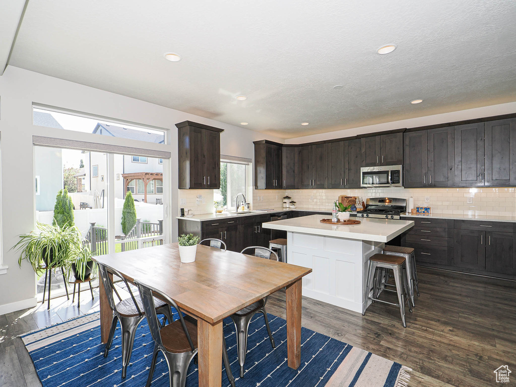 Kitchen featuring stainless steel appliances, light countertops, a kitchen island, tasteful backsplash, and dark brown cabinets