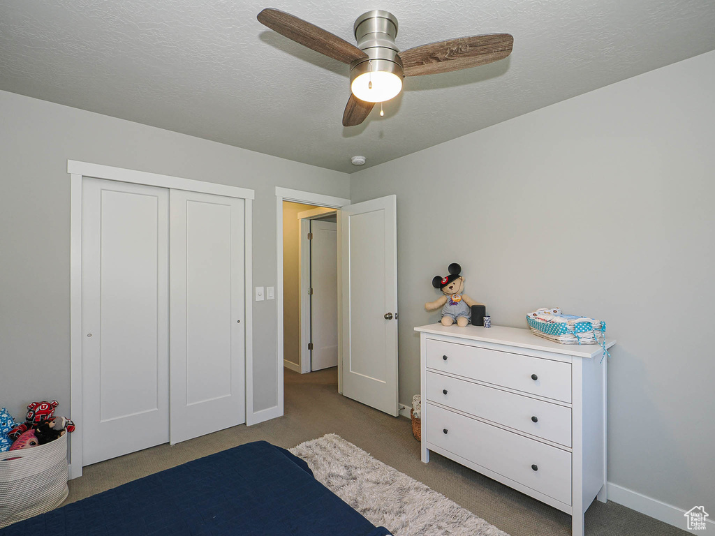 Carpeted bedroom with baseboards, ceiling fan, and a closet