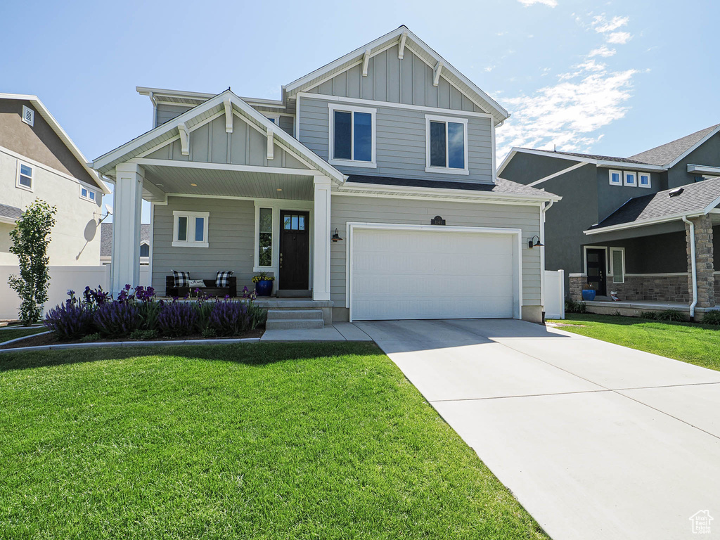 Craftsman inspired home with board and batten siding, covered porch, a garage, and a front lawn
