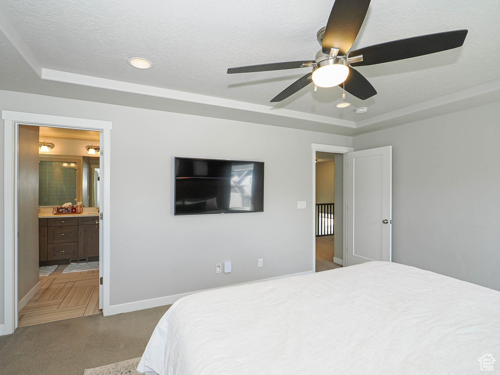 Carpeted bedroom with a tray ceiling, baseboards, ensuite bath, ceiling fan, and recessed lighting