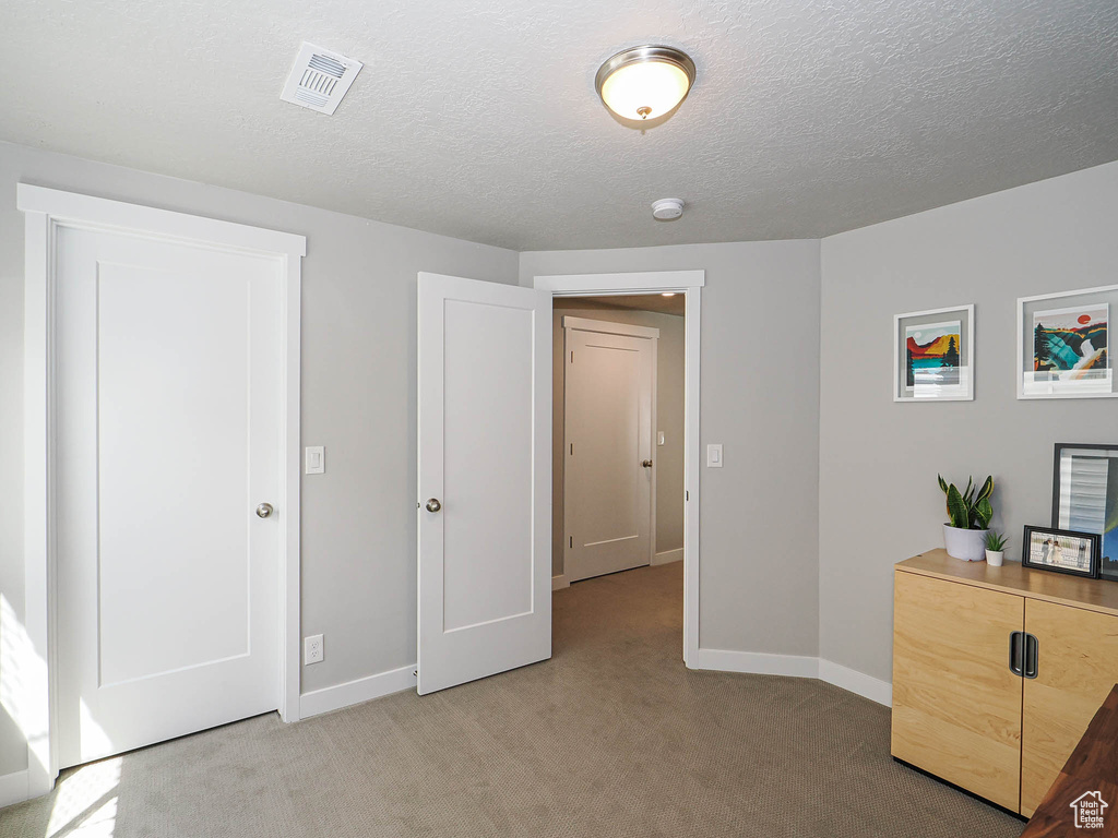 Unfurnished bedroom featuring light colored carpet, baseboards, and a textured ceiling