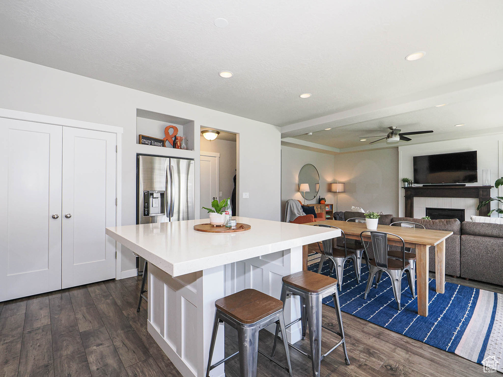 Kitchen with dark wood-style floors, stainless steel fridge, a breakfast bar area, a center island, and recessed lighting