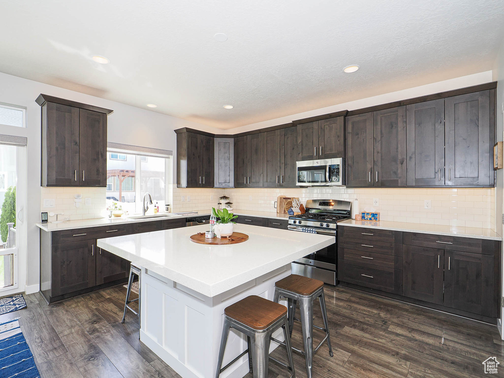 Kitchen with stainless steel appliances, a breakfast bar area, a sink, dark brown cabinetry, and dark wood finished floors