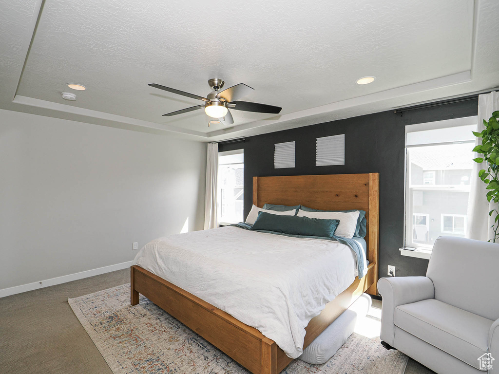 Carpeted bedroom with a tray ceiling, baseboards, a textured ceiling, recessed lighting, and ceiling fan