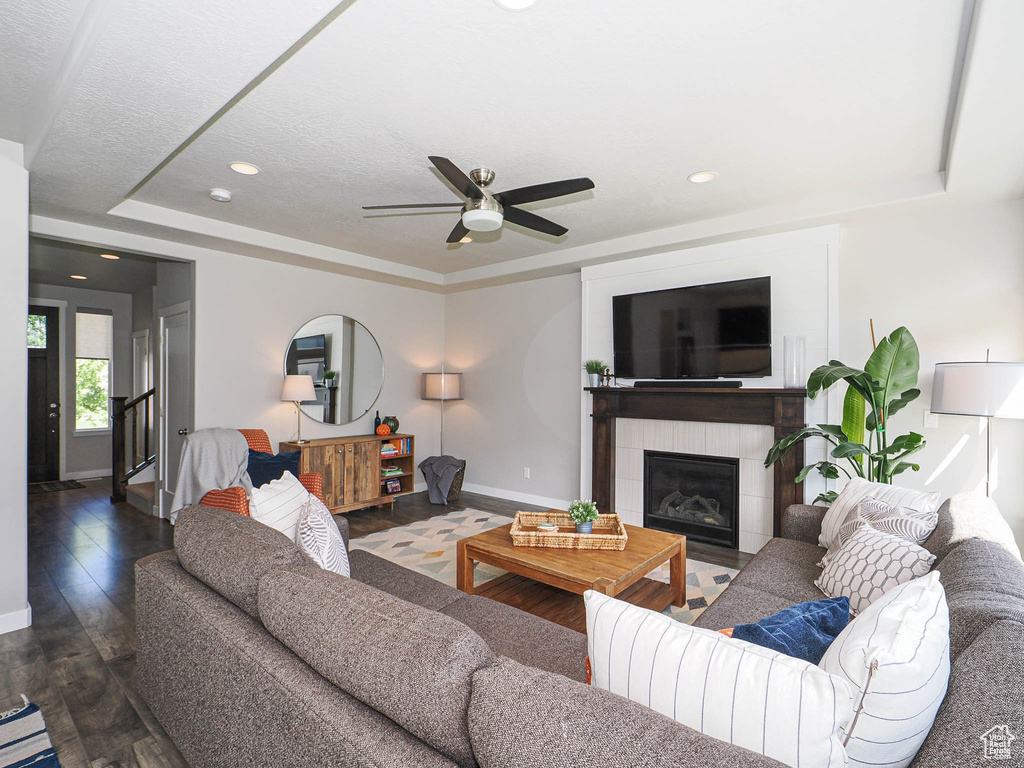 Living room featuring baseboards, a raised ceiling, a ceiling fan, a fireplace, and wood finished floors