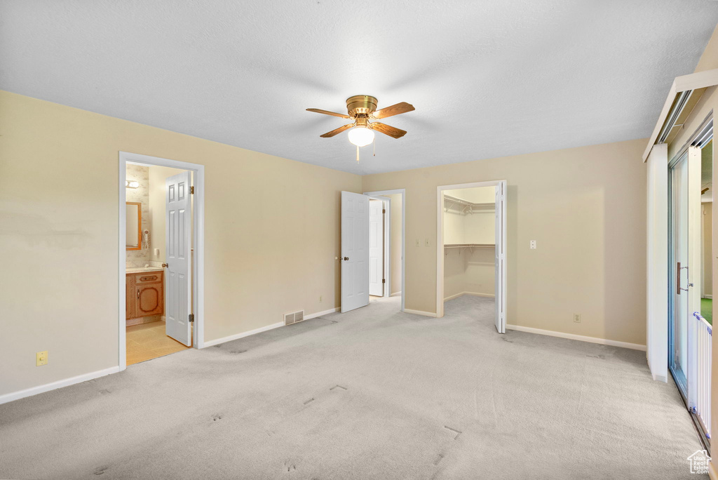 Unfurnished bedroom featuring light colored carpet, baseboards, a walk in closet, a closet, and ensuite bathroom