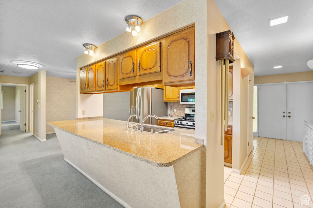 Kitchen featuring stainless steel appliances, a sink, brown cabinets, and a peninsula