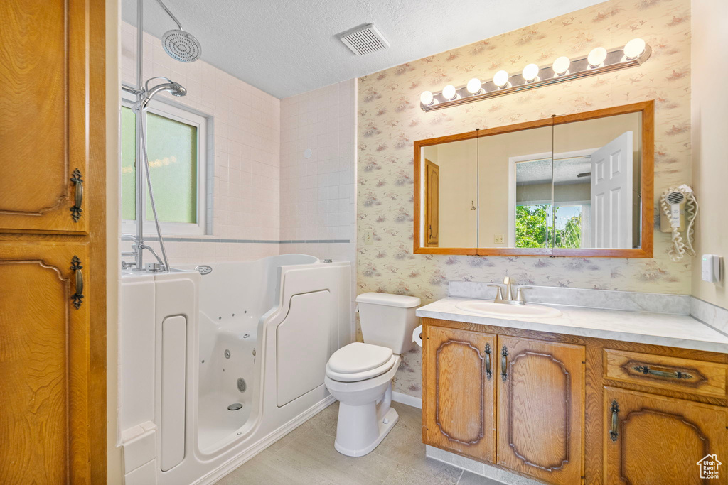 Bathroom with wallpapered walls, a whirlpool tub, vanity, toilet, and a textured ceiling