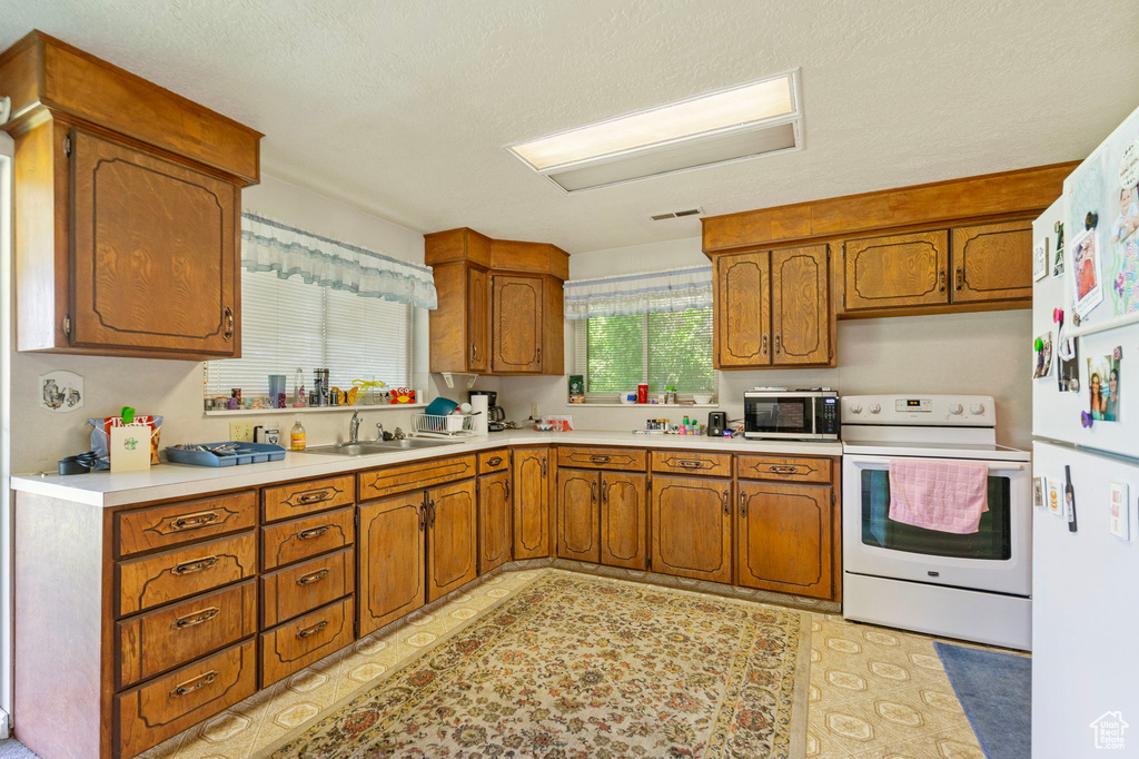 Kitchen with white appliances, a sink, brown cabinets, light countertops, and a textured ceiling
