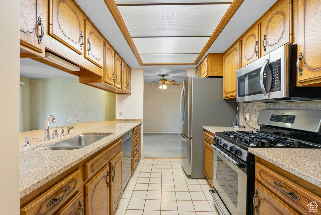 Kitchen with appliances with stainless steel finishes, a sink, brown cabinets, and light tile patterned floors