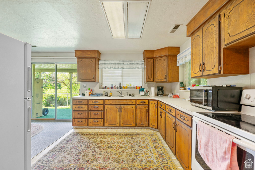 Kitchen with white appliances, light countertops, brown cabinets, a sink, and a textured ceiling
