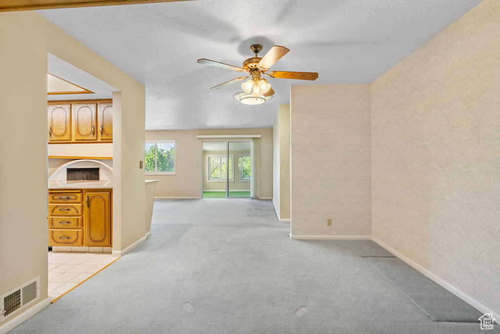 Unfurnished living room with carpet floors, a ceiling fan, a textured ceiling, and baseboards