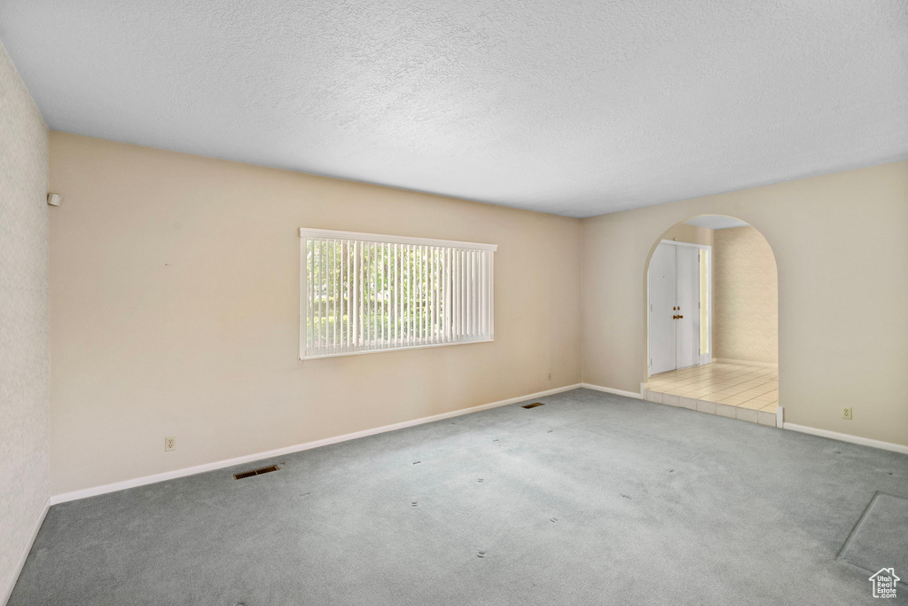 Empty room with arched walkways, carpet, baseboards, and a textured ceiling