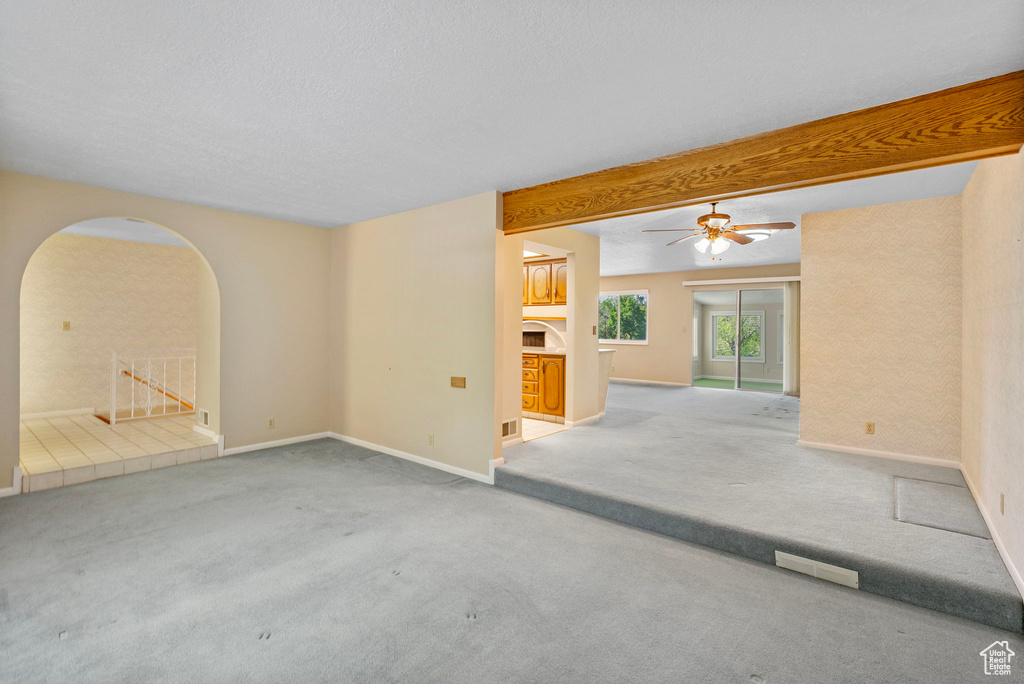 Spare room with arched walkways, carpet, baseboards, ceiling fan, and beamed ceiling