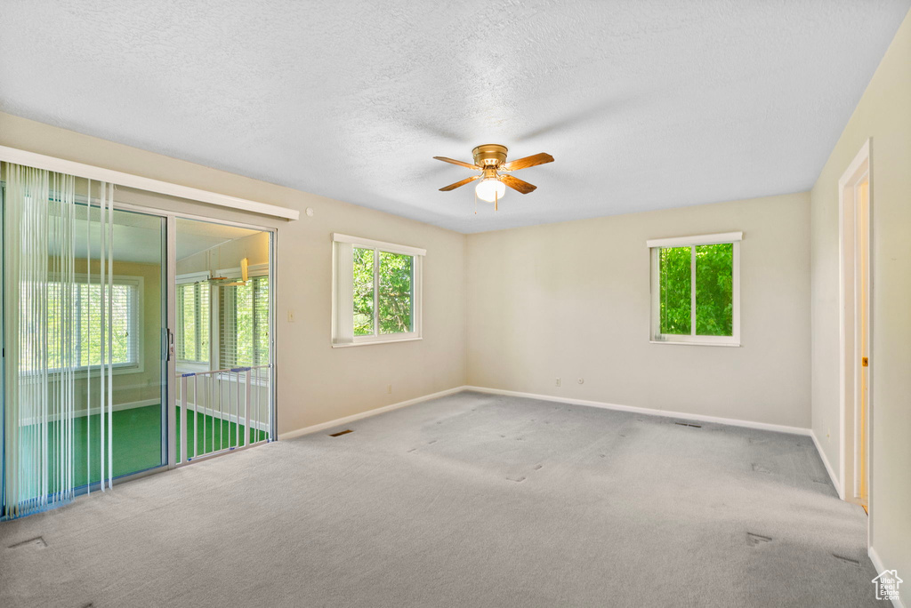 Carpeted spare room featuring baseboards, ceiling fan, healthy amount of natural light, and a textured ceiling