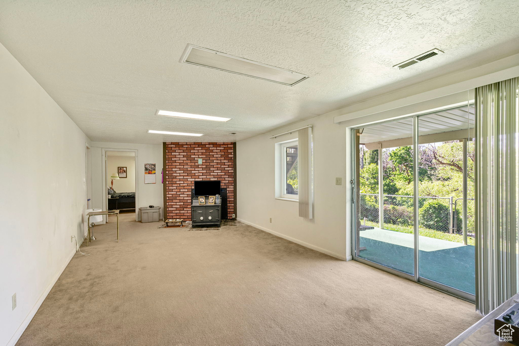 Unfurnished living room featuring attic access, carpet, a textured ceiling, and baseboards