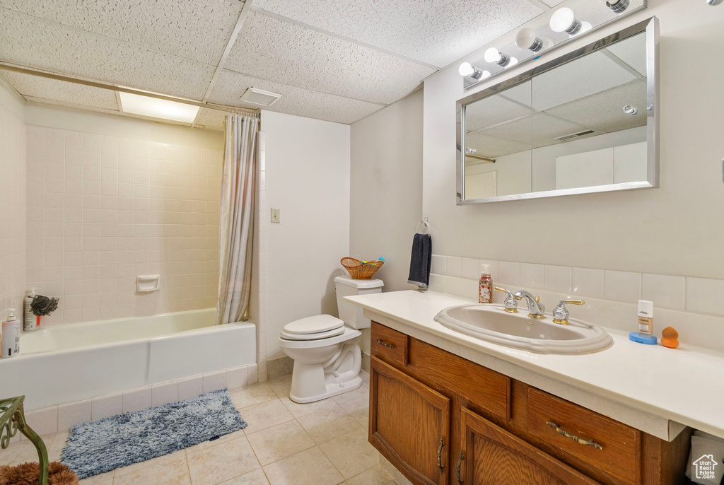 Bathroom featuring toilet, vanity, tile patterned floors, a drop ceiling, and shower / tub combo