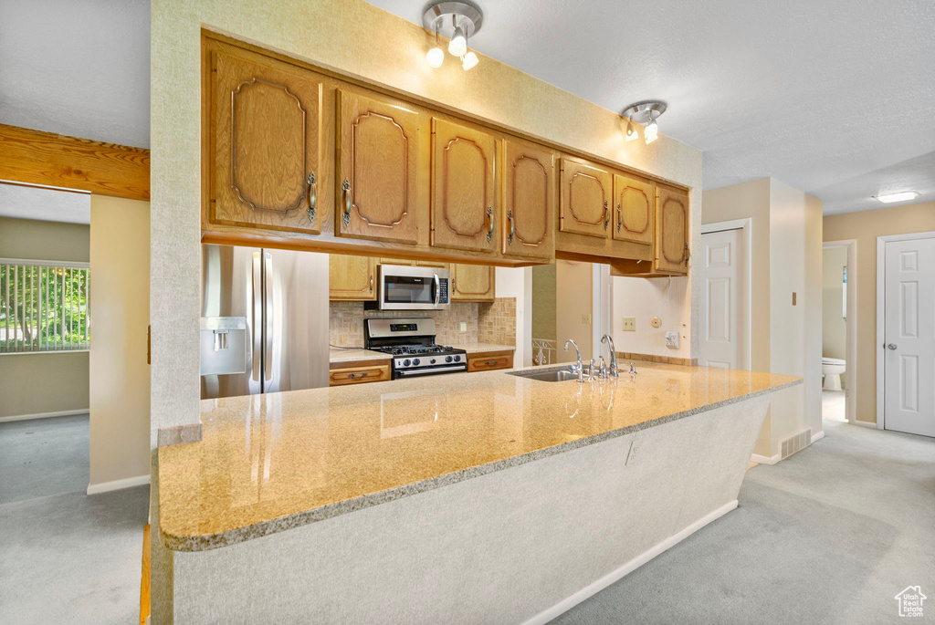 Kitchen featuring stainless steel appliances, a sink, baseboards, decorative backsplash, and light stone counters