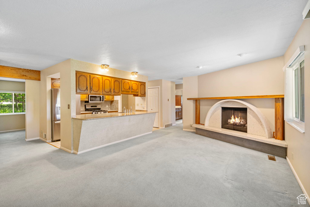 Unfurnished living room featuring light carpet, baseboards, a lit fireplace, and a sink