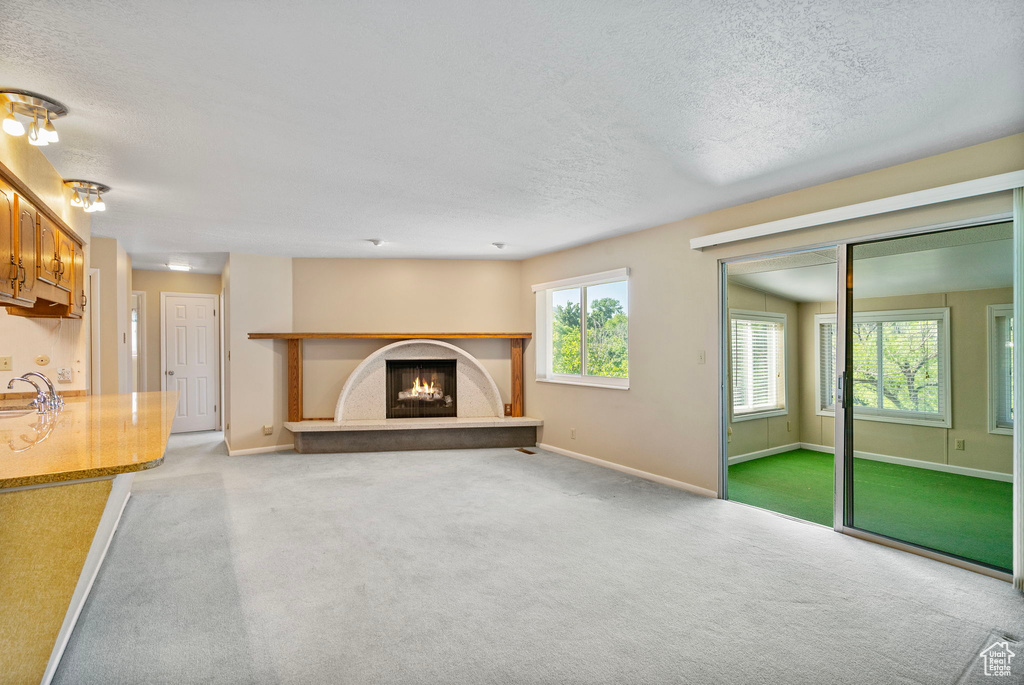 Unfurnished living room featuring carpet flooring, a sink, a textured ceiling, a warm lit fireplace, and baseboards
