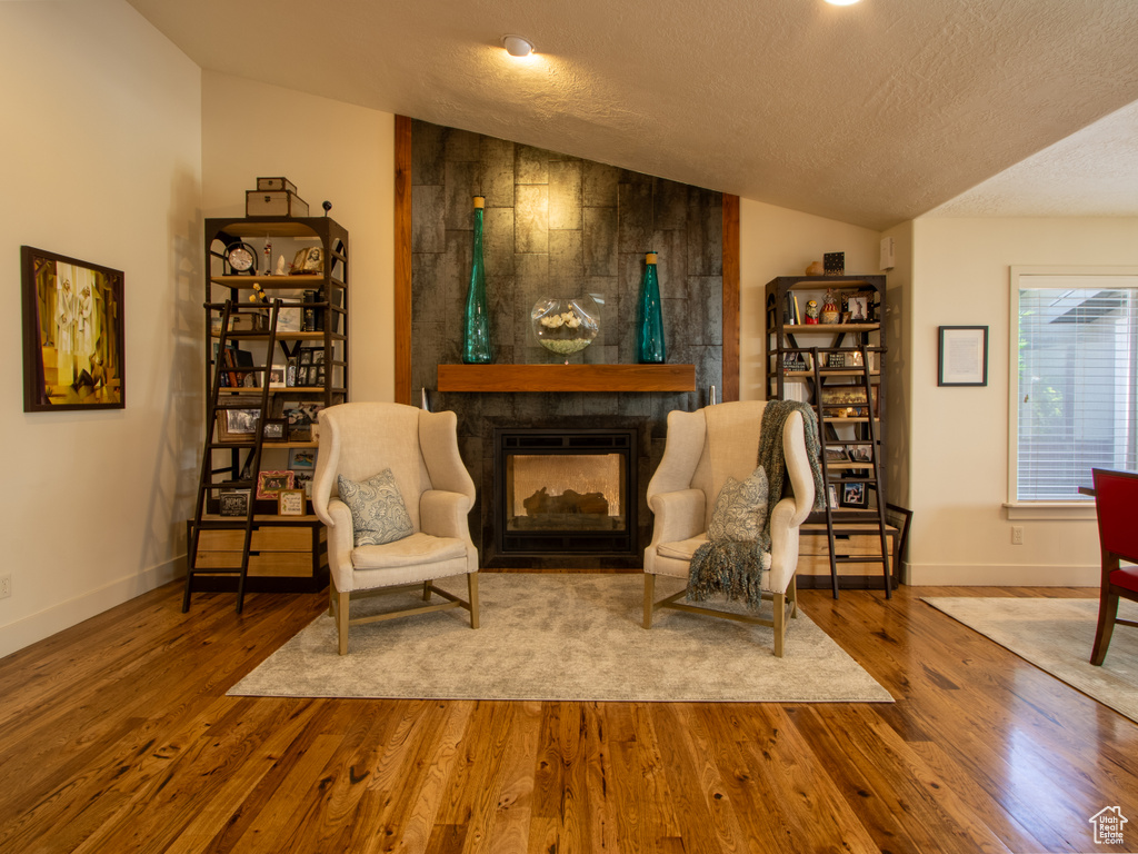Sitting room featuring wood finished floors, baseboards, a fireplace, a textured ceiling, and lofted ceiling