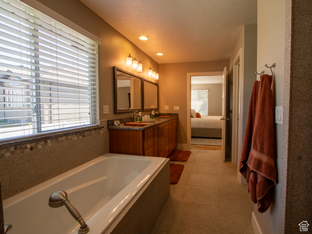 Ensuite bathroom featuring double vanity, a bath, a textured ceiling, recessed lighting, and baseboards