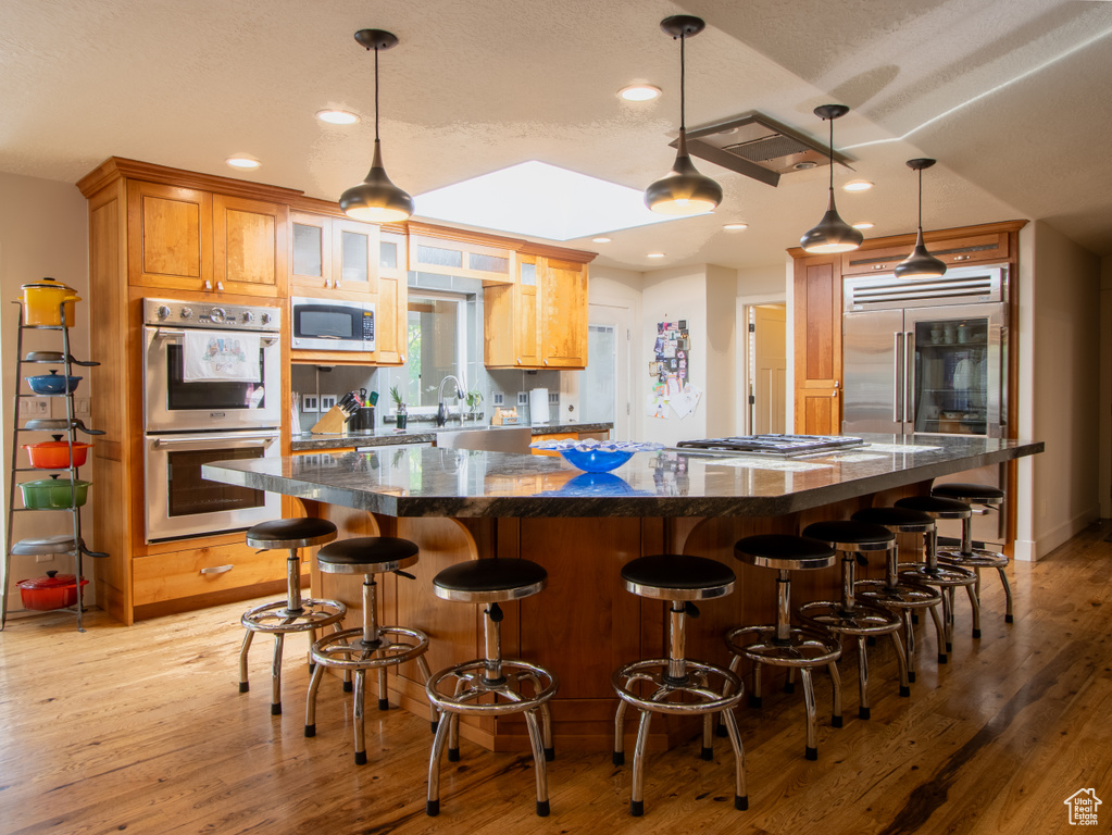 Kitchen featuring appliances with stainless steel finishes, a spacious island, light wood-style floors, a kitchen bar, and decorative light fixtures
