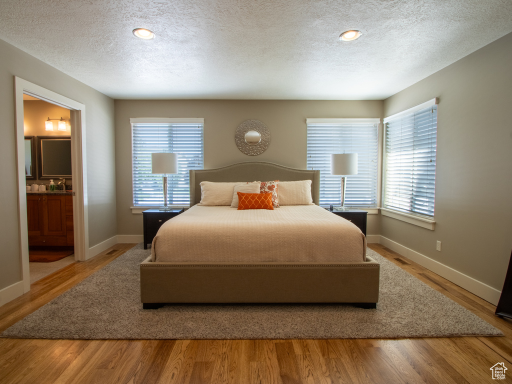 Bedroom featuring baseboards, connected bathroom, a textured ceiling, and wood finished floors