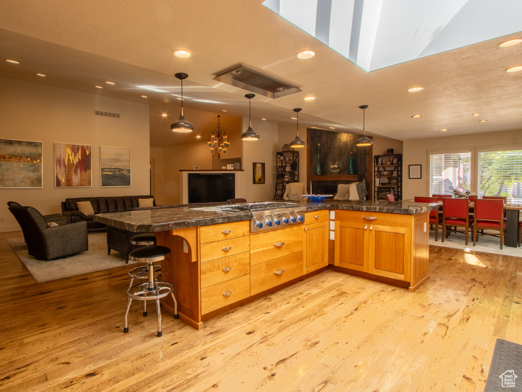 Kitchen featuring stainless steel gas stovetop, open floor plan, recessed lighting, light wood finished floors, and a breakfast bar