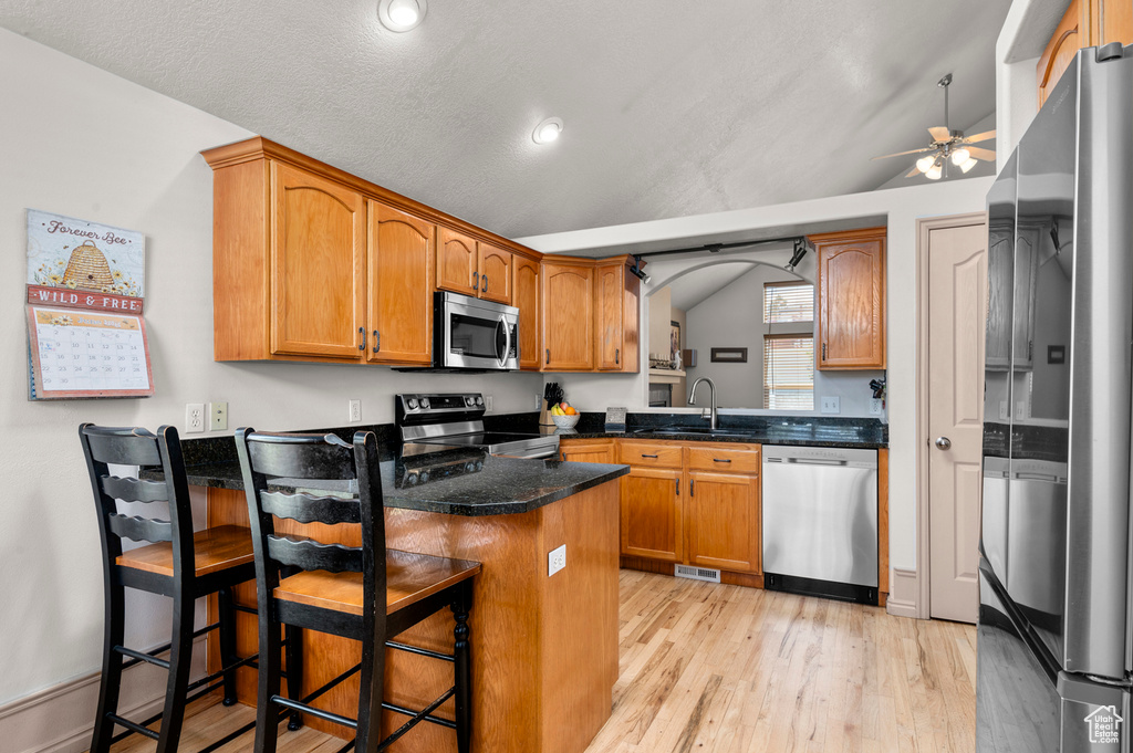 Kitchen with appliances with stainless steel finishes, a sink, a ceiling fan, light wood-type flooring, and a peninsula