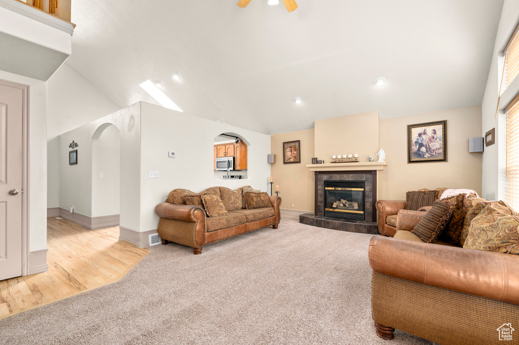 Living area featuring light carpet, arched walkways, lofted ceiling, a tile fireplace, and recessed lighting