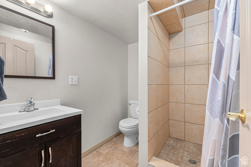 Full bath featuring vanity, toilet, tiled shower, and baseboards