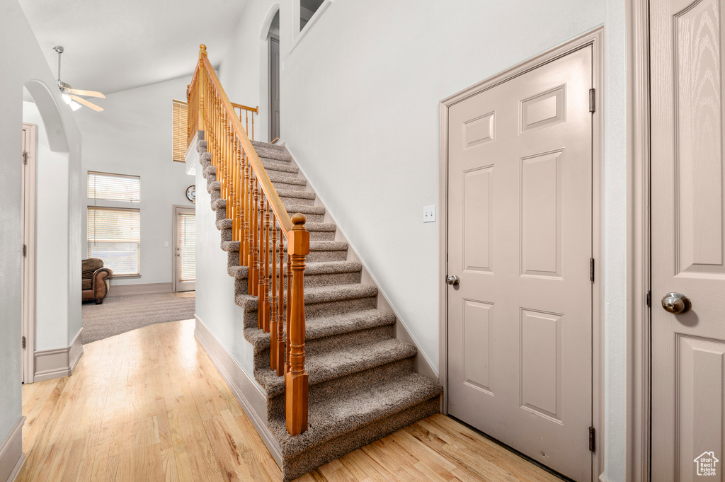 Staircase with arched walkways, wood finished floors, a ceiling fan, a towering ceiling, and baseboards