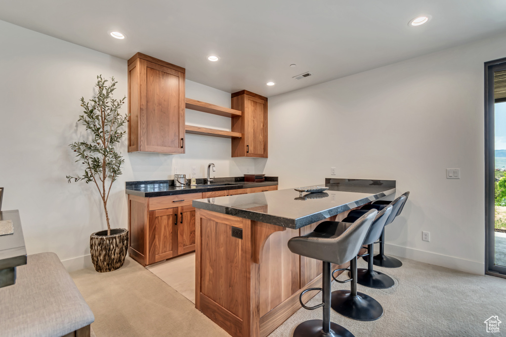 Kitchen with light colored carpet, open shelves, a breakfast bar, recessed lighting, and a sink