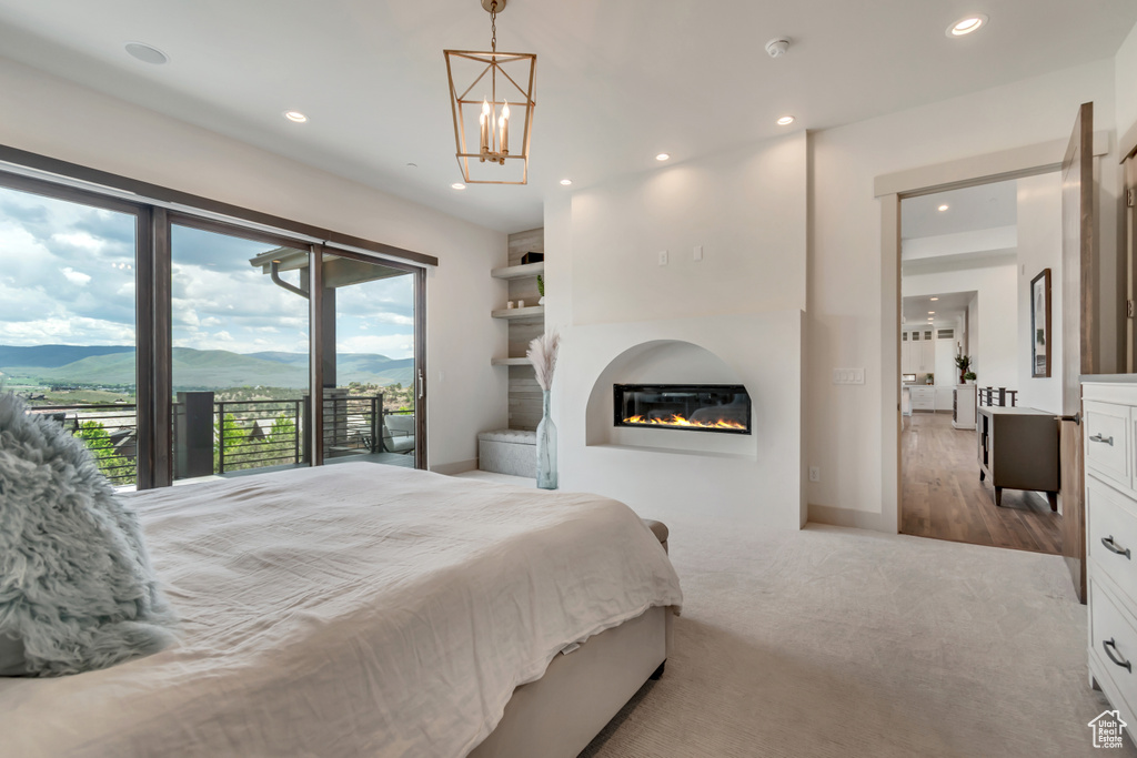 Carpeted bedroom with access to exterior, recessed lighting, a glass covered fireplace, a mountain view, and a chandelier