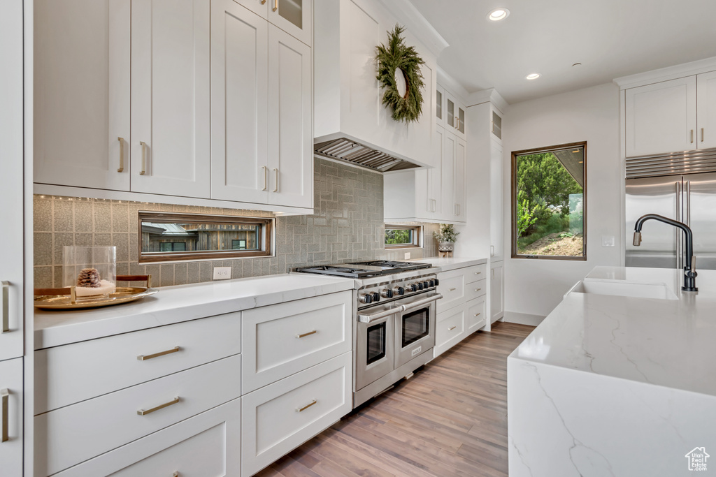 Kitchen featuring premium appliances, a sink, custom range hood, light wood-style floors, and recessed lighting