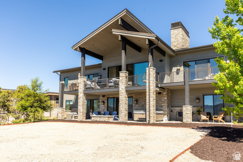 View of front of house featuring a balcony, stone siding, a chimney, and a patio